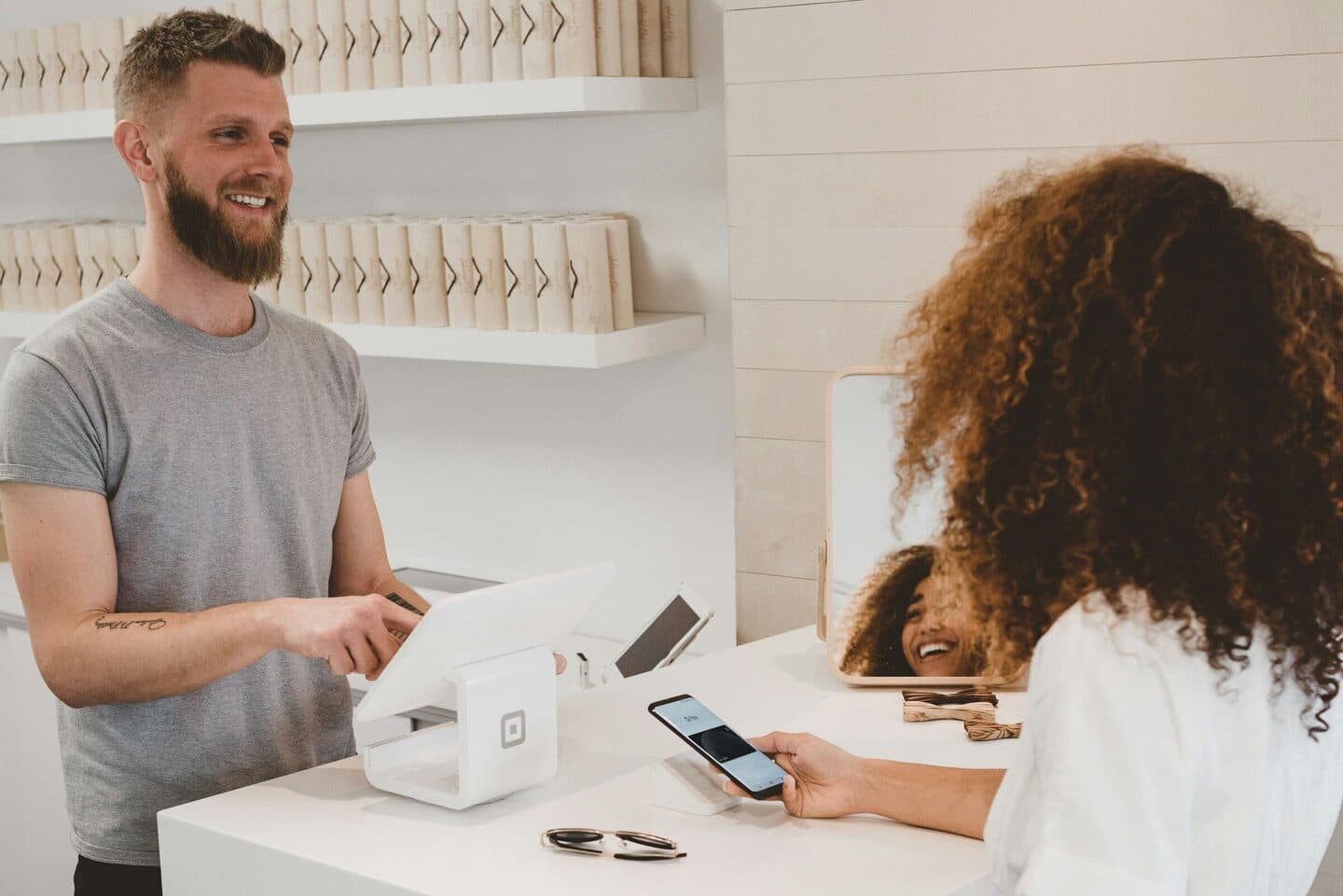 Sales assistant at the till smiles at a customer paying with her phone