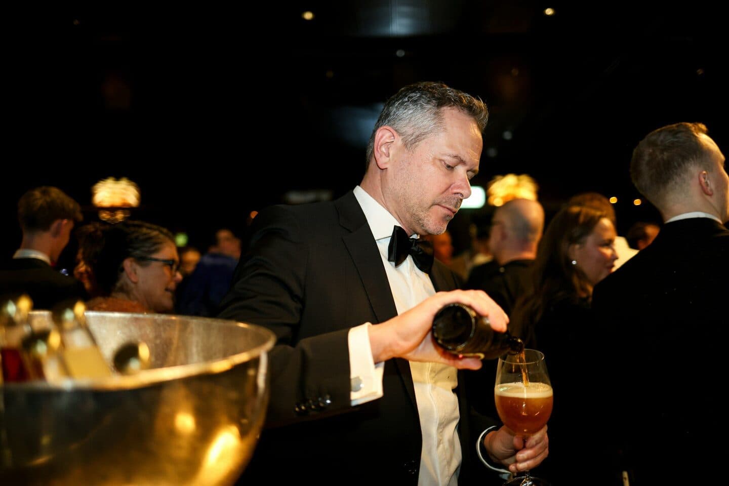 Man in a tuxedo pours a beer at a gala