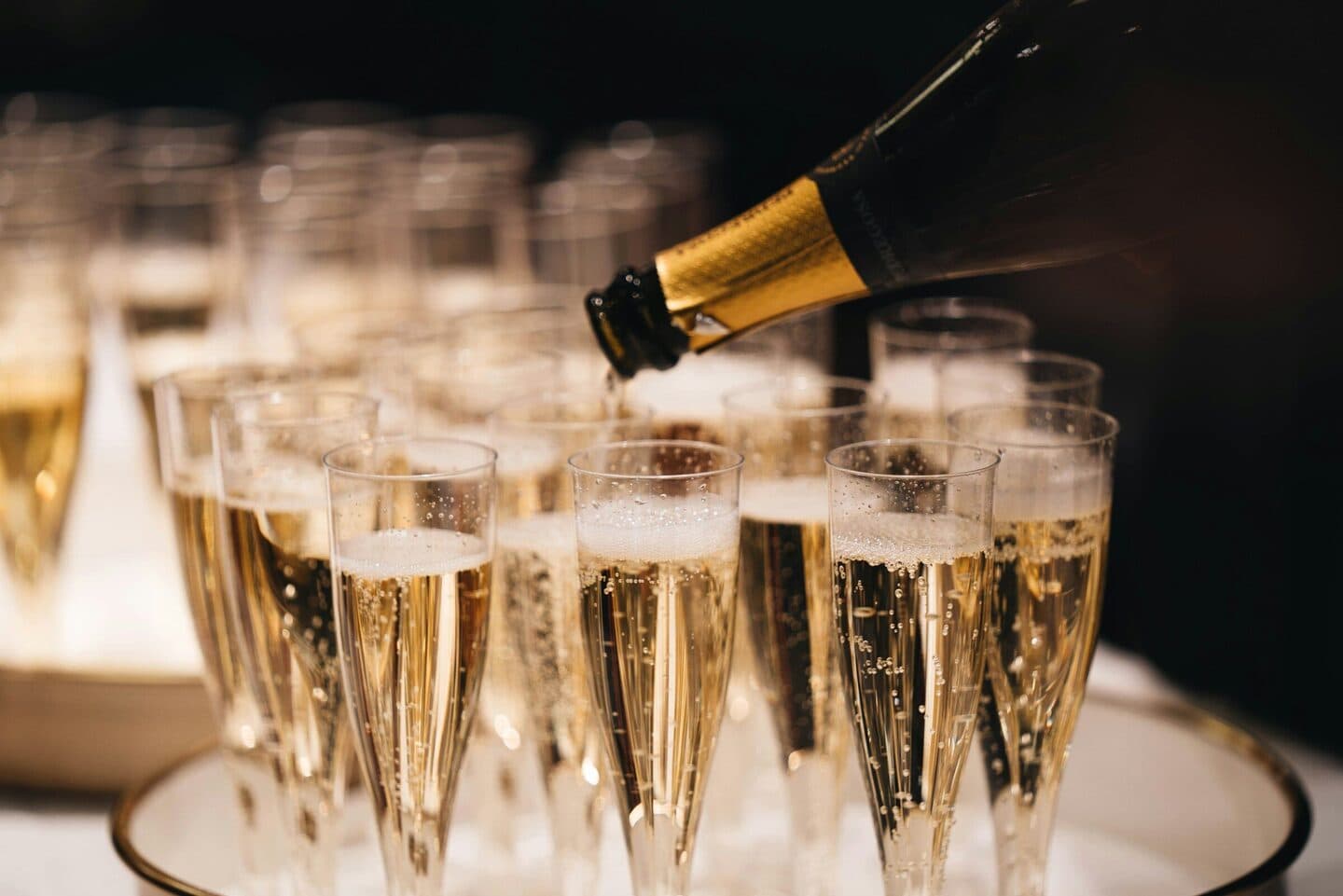 Sparkling wine is poured into a row of glasses on a tray