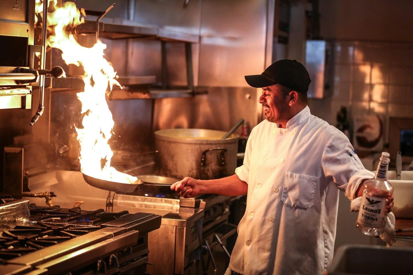 Cook tosses a pan with a burst of flame at the stove of a restaurant kitchen