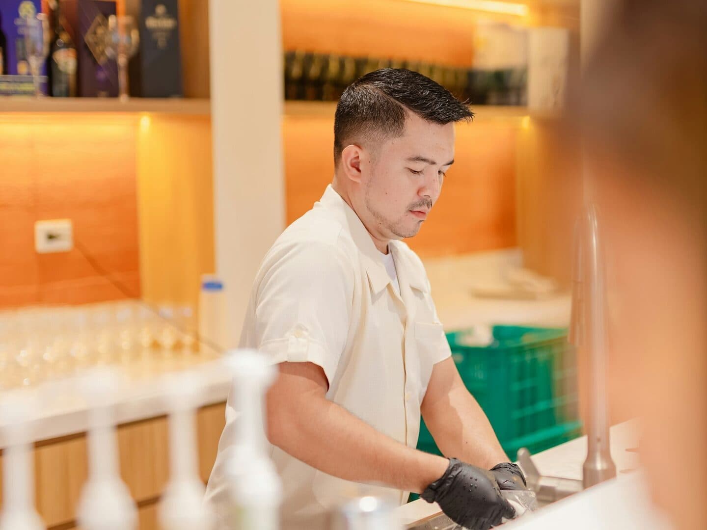 Man wearing gloves washes glasses at a counter